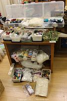 Photo showing large assortment of crafting trims, ribbons, lace, and sewing threads organized on and around a table in plastic boxes and containers.