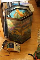 Two hexagonal glass aquariums with black edging, stacked together, with an aquarium heater and cords leaning against them, partially visible aquarium supplies and gardening items around them.