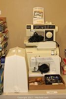 Two vintage sewing machines stacked; Kenmore Sonata Model 6606 on top and Singer below, with manual and some accessories.