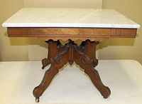 Front view showing marble top and wooden base with decorative carving and casters on feet.