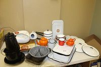 Overview photo showing the entire collection of various vintage enamelware including coffee pot, teapots, baking pans, cups, colander, and trays on a table.
