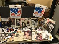 Wide view of collection showing various signed and unsigned country music magazines and programs scattered on table with The Statler Brothers promotional bags.