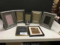 Eight decorative metallic photo frames displayed on a table in two rows, showing various sizes and intricate borders