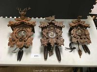 Three carved cuckoo clocks laid side by side on table, showing overall lot contents.