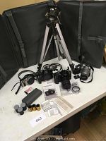 Full lot showing three Canon cameras, Kenlock flash, tripod, various accessories, and film rolls on a white table.