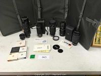 Wide view of six lenses arrayed with cases, lens caps, manuals, and filters on table.