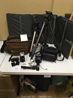 Full view of all items on table including two tripods, two camera bags, Sunpak and Quantaray flashes, flash mounts and accessories.