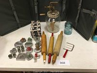 Full view of all items on a white table including the butter churn, rolling pins, soap boxes, cookie cutters and dough blender.