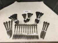 Full set of flatware pieces arranged on table including knives, forks, spoons, and smaller spoons all with matching embossed ornate handles.