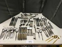 Wide angle photo of entire flatware collection laid out in groups on table inside open carrying case. Various types of cutlery visible sorted by type with some gold tone pieces in front right.