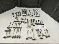 Overview photo showing over 70 pieces of silver plate flatware arranged on a flat surface with various spoon, fork, and serving utensil types visible.