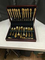 Full set of gold electroplated flatware neatly arranged in wood storage box showing knives, forks, spoons.