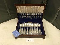 Full view of open wooden box showing neatly arranged silverplate flatware in original packaging in blue velvet lining.