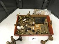 Various antique household hardware spread in a box showing brass faucets, porcelain knobs, metal plates and fittings