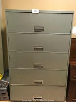 Green metal vertical file cabinet with five drawers seen from the front.