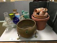 Wide view of the lot showing brass footed planter, terracotta pots stacked inside a large terracotta pot, and various glass and ceramic planters grouped on table.