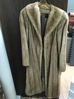 Full view of the vintage fur coat hanging on hanger showing its length and light brown fur exterior.