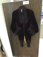 Full view of antique Victorian jet glass beaded velvet jacket hanging on wood background showing front with loose tails and puffed sleeves.