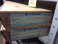 Two cardboard boxes on shelves labeled Commander QM32125 breaker panels, showing product specifications and packaging details.