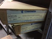 Two stacked boxes on shelving labeled Commander QM32125 breaker panels, model number and specifications visible.