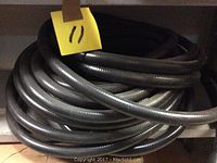 Close-up photo showing the black ribbed flexible conduit coil with a yellow tag labeled '11' placed on top.