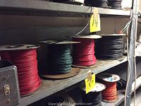 Four spools of assorted colored wire placed on metal shelving showing red, green, black wires with yellow lot tags.
