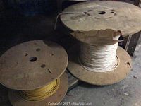 Two wooden spools of wire, one yellow and one white with colored stripes, placed on the floor.