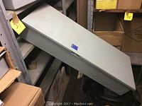 Top angled side view of gray metal breaker panel inside storage shelf.