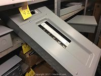 Top view showing one gray metal breaker panel with closed hinged breaker slot cover and several mounting knockouts on the side.