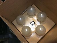 Five glass globes with bubble texture arranged in a circle inside cardboard box, centered around the fixture socket.