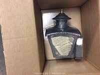Black metal lantern-style outdoor light fixture in its original box.