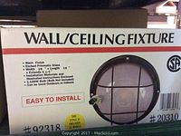 Boxed wall/ceiling light fixture showing product details and image of fixture with black finish, etched prismatic glass, dimensions, and installation notes.