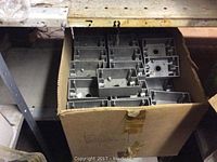 Cardboard box filled with multiple gray metal electrical boxes, each with mounting holes and cutouts for wiring.