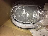 Ceiling fixture inside plastic wrap showing round white frame and glass diffuser.