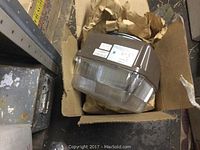 Two Powerlite 70W high pressure sodium lighting fixtures in a box with brown packing paper.