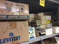 Metal shelving units containing approximately 50 boxes of Leviton toggle switch plates and electrical plates in original packaging.