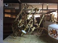 Brass hanging light fixtures with white and floral-patterned glass shades on metal shelving.