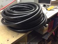Coiled roll of black flexible corrugated conduit on a workbench surface.