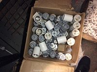 Box filled with large electrical sockets primarily white and blue-gray in color, stacked loosely