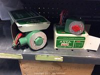 Two green ASCO Red-Hat solenoid valves with wiring visible, set inside open ASCO boxes on a shelf.