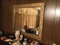 Front view of the large wall mirror hung on a wood-paneled wall showing full frame and reflection.