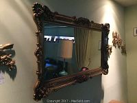 Full view of the large rectangular wall mirror with gold trim and attached floral and scroll decorative elements on the corners.