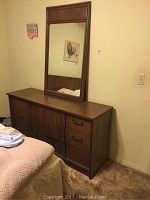 Full view of the wooden dresser with mirror mounted on the wall above it in a bedroom setting.