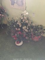 Photo showing multiple faux flower arrangements in ceramic pots against a light green wall and carpeted floor.
