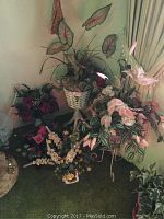 Photo showing multiple faux plants arranged indoors on green carpet, including tall leafy plant on white wicker basket stand and several colorful floral bouquets on metal stands and pots.
