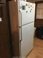 Front and side view of white Maytag top freezer refrigerator in a room with wood paneling and hardwood floors, showing general condition and overall appearance.