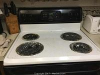 Front view of a white electric stove with black coil burners and control panel, showing signs of use.