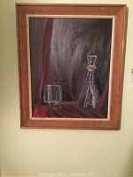 Framed oil painting of a glass and decanter against a dark curtain background