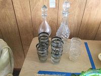 Two glass wine decanters, six regular round clear glasses with silver and black monogram bands, and two smaller textured clear glasses arranged on a table.