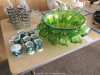 Green glass punch bowl with matching ladle and hanging cups, miniature espresso cups and sugar bowl displayed on table.